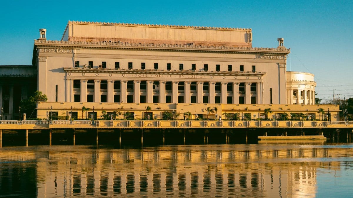 Capture of the iconic Manila Post Office, reflecting in the tranquil Pasig River under a clear sky.