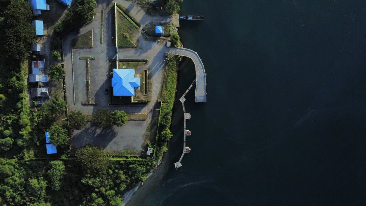 Drone capture of a lakeside property with blue-roofed buildings and a dock in a scenic landscape.