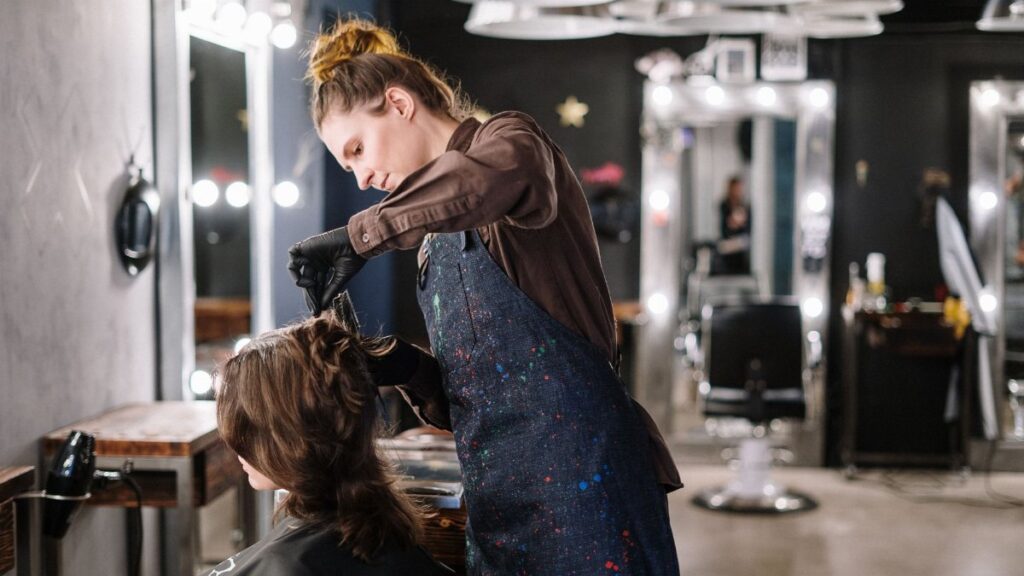 A female stylist expertly applying hair color to a client in a modern salon setting.