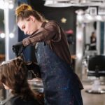 A female stylist expertly applying hair color to a client in a modern salon setting.