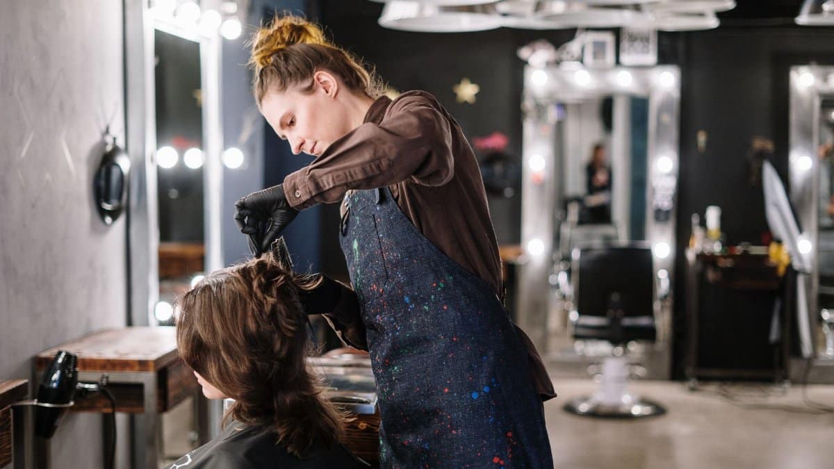 A female stylist expertly applying hair color to a client in a modern salon setting.