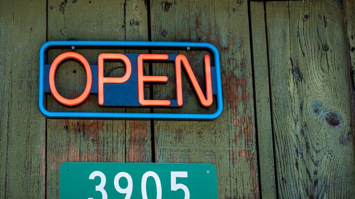 Close-up of a red neon open sign and address on rustic wooden wall.