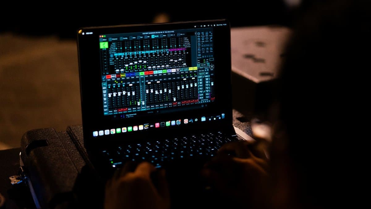 A sound engineer adjusting audio settings on a digital mixer via a laptop.