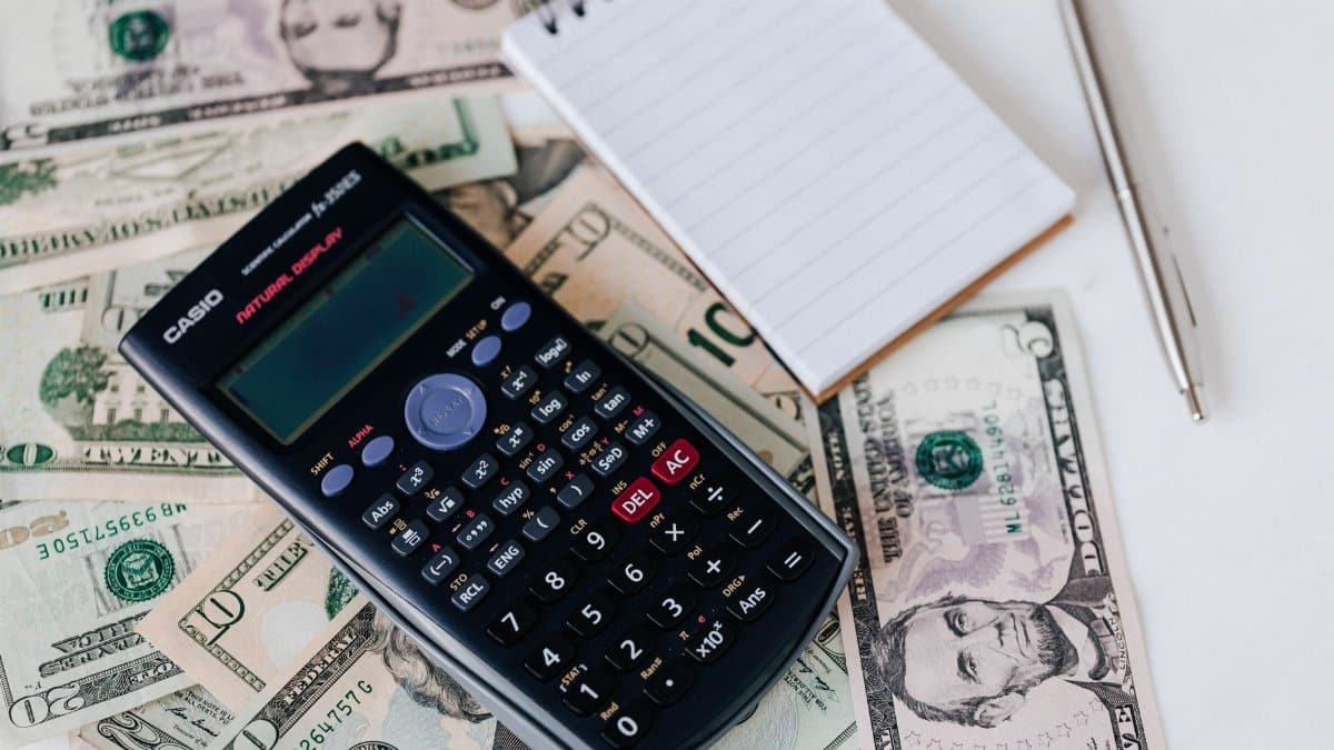 From above electronic calculator and notepad placed over United States dollar bills together with metallic pen for budget planning and calculation