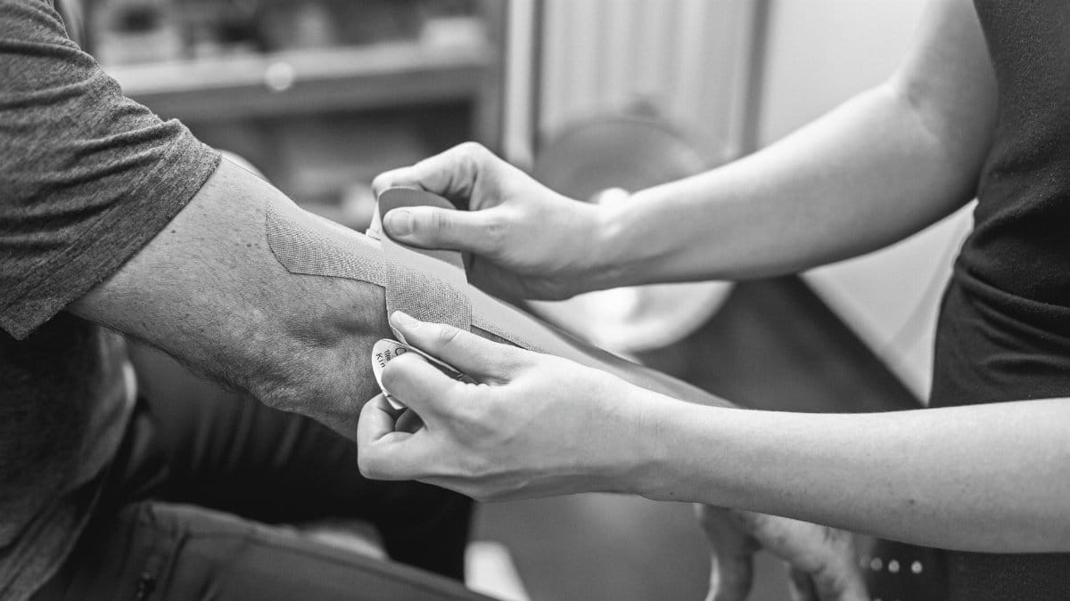 Close-up of kinesiology tape being applied on an elbow for therapeutic support in a healthcare setting.