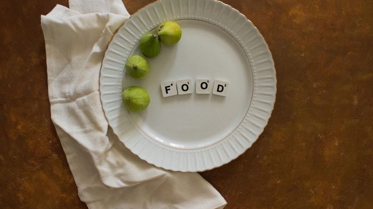 Top view of a white plate with figs and arranged food text on a rustic surface.