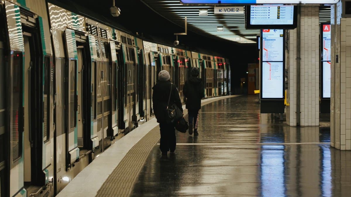 Two passengers walking at a Paris subway platform, under a 'Sortie' sign, with train in view.