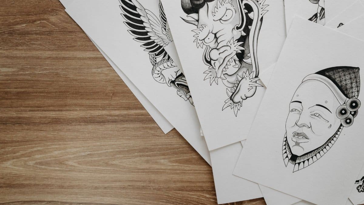 Top view of detailed black and white drawings on paper arranged on a wooden table.