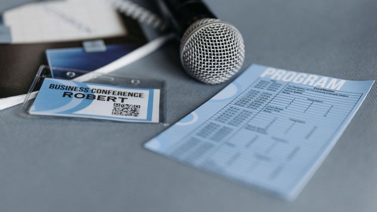 Close-up of a microphone, name tag, and program guide on a table at a business conference.