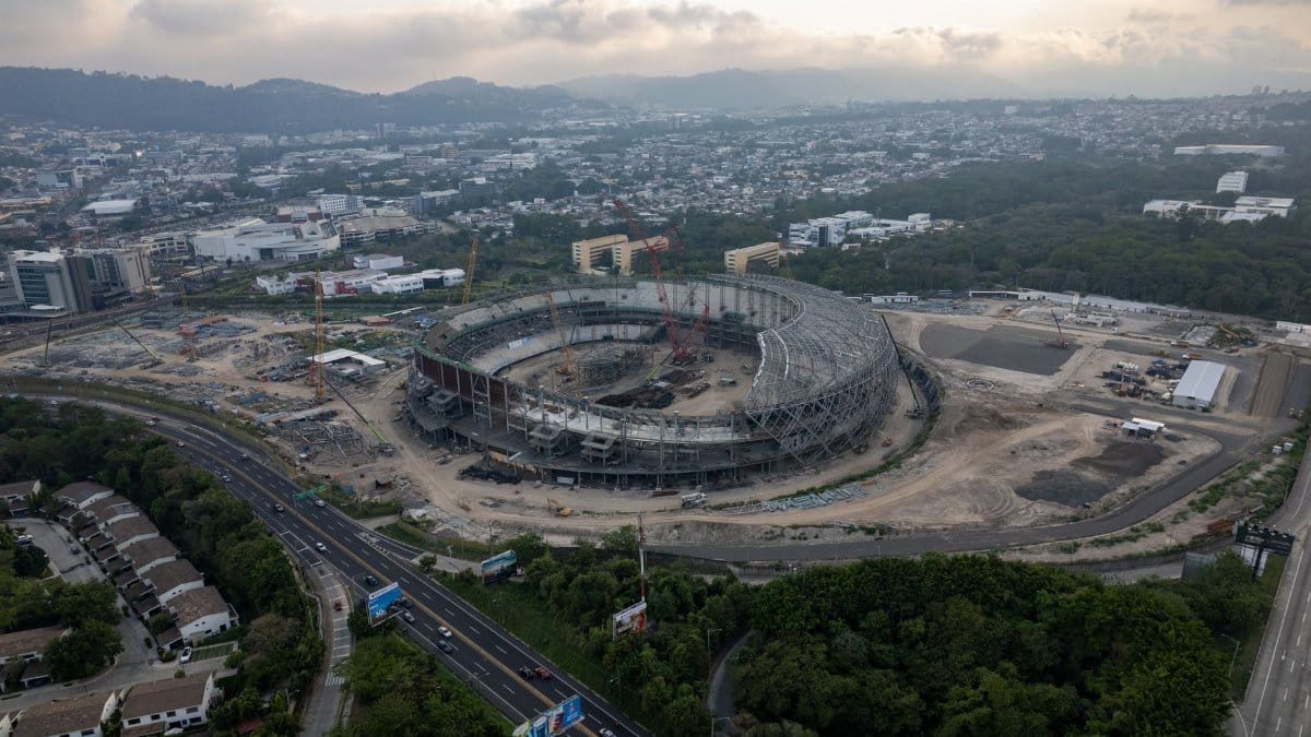Aerial view of a large stadium under construction amidst a sprawling urban landscape.