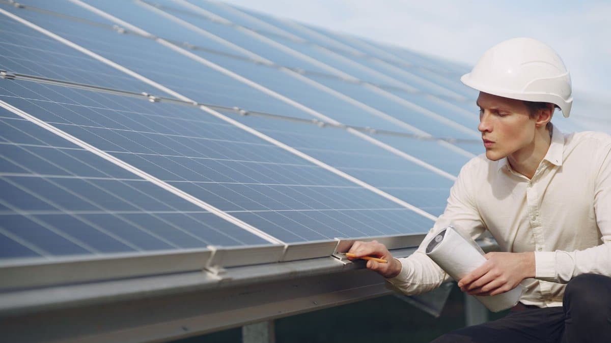 Focused young male employer in formal wear and hardhat working on solar panel station and checking details of modules