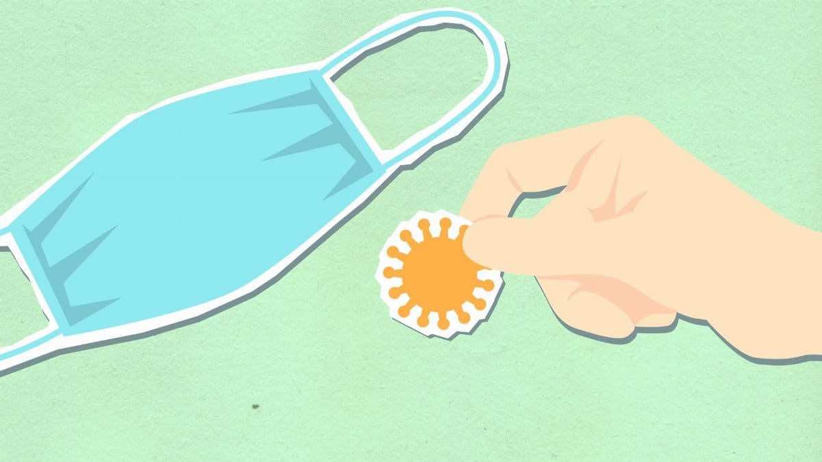 Decorative cardboard illustration of hand with virus near disposable mask during coronavirus pandemic on green background