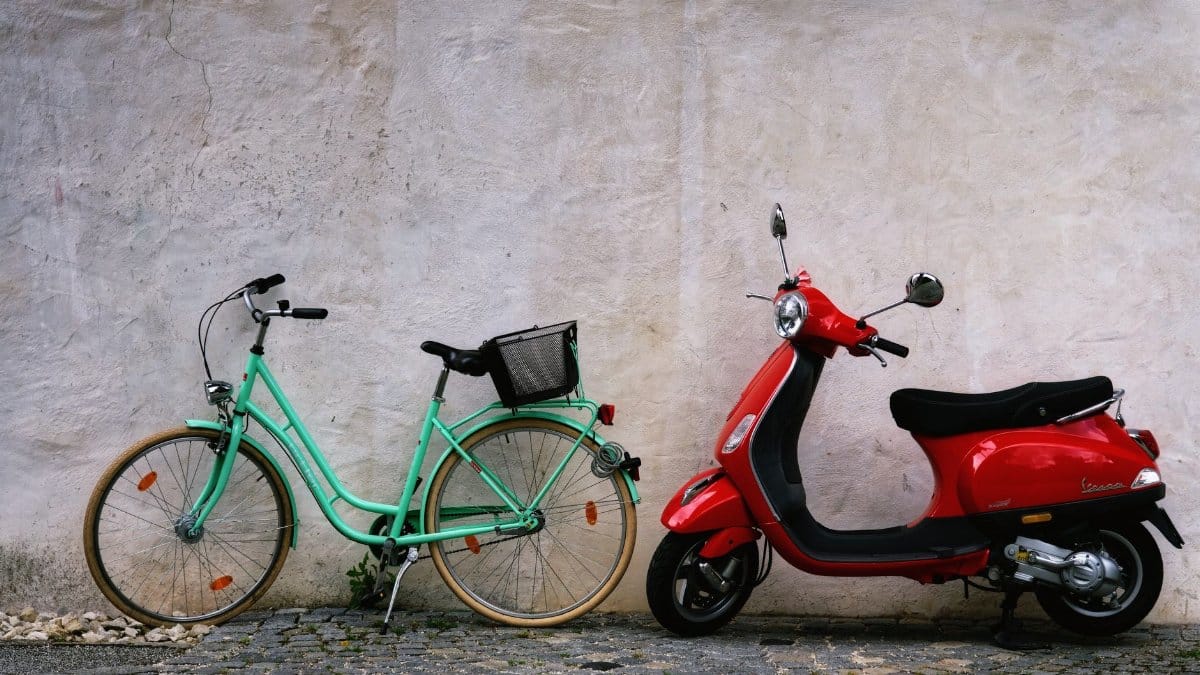 Parked bicycle and scooter side by side in front of a rustic wall, showcasing urban transportation options.