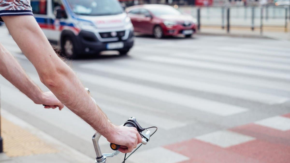 A cyclist pauses at a crosswalk in Warsaw, Poland, with an ambulance in the background.