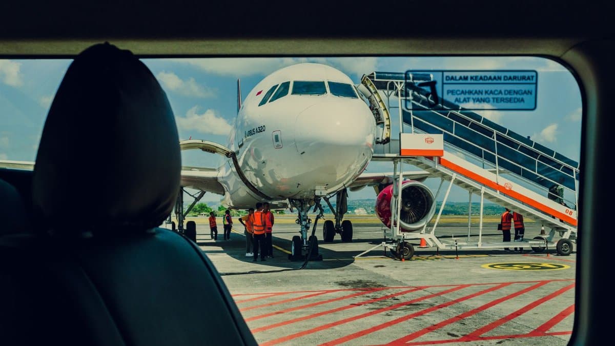 Airplane viewed from a car, parked on the tarmac at an airport with crew working nearby.