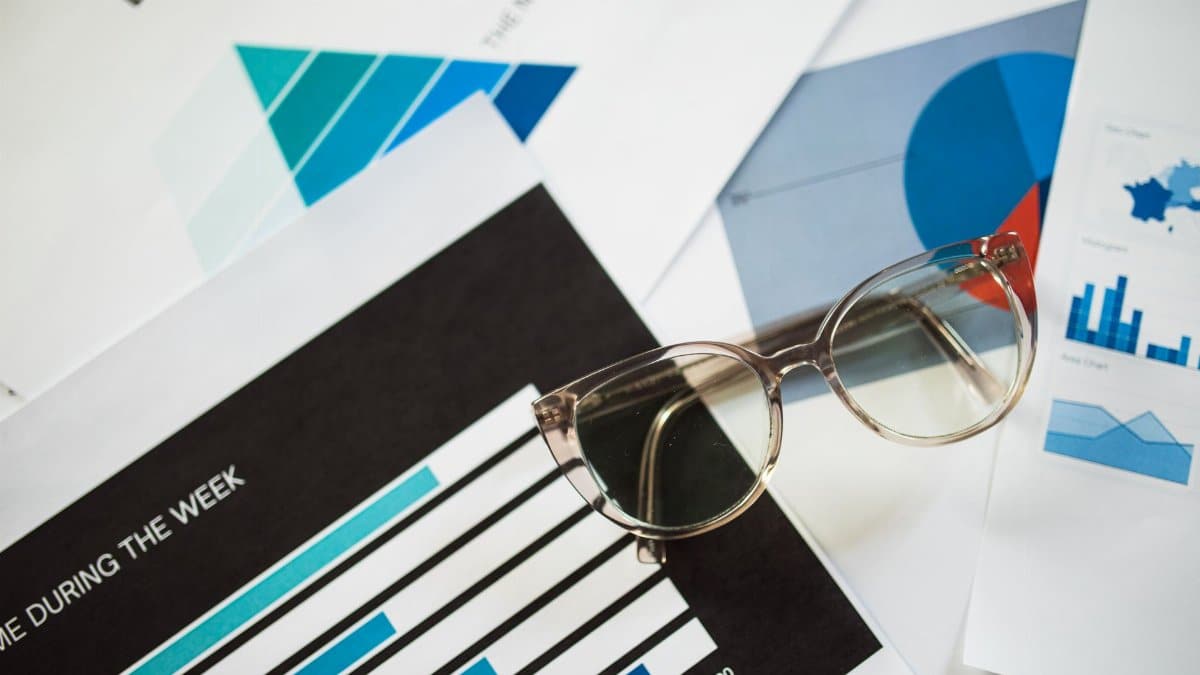 Close-up of eyeglasses resting on financial documents with various charts and graphs.