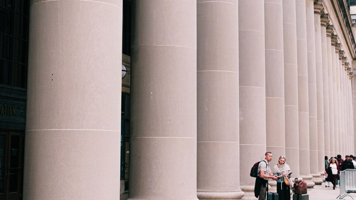 Two travelers stand beside large columns in Chicago, capturing the essence of urban exploration and architectural beauty.