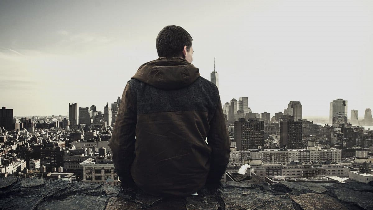 Man sitting on rooftop overlooking city skyline, contemplating the urban landscape.