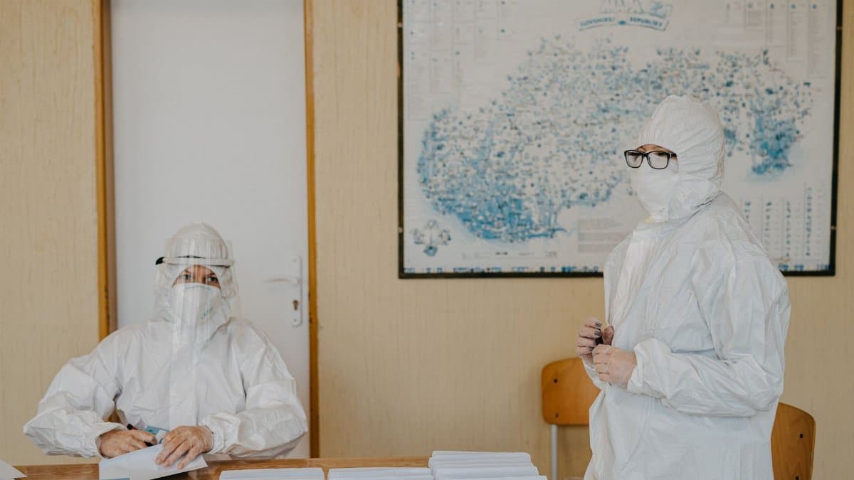 Healthcare workers in protective gear working indoors amid pandemic setting.