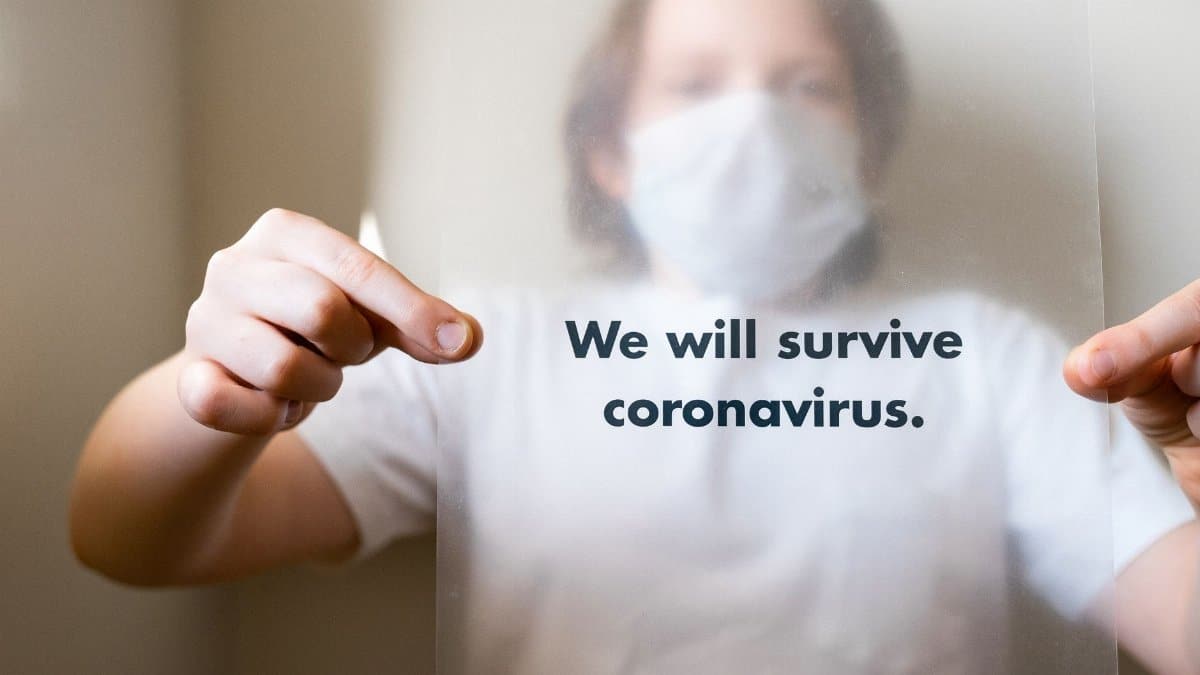 A person with a mask holding a sheet with 'We will survive coronavirus' message.