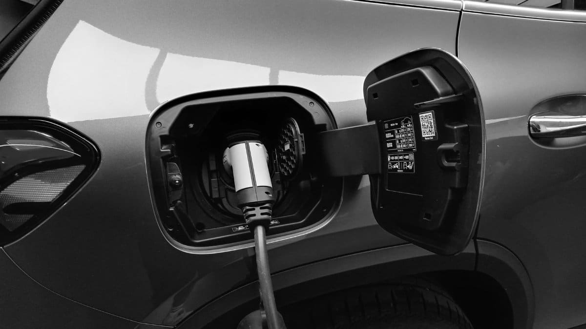 Close-up black and white image of an electric vehicle charging at a station.