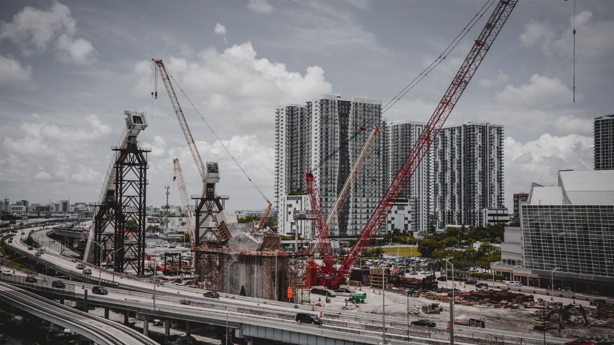 A cityscape featuring high-rise buildings and a construction site with cranes under a cloudy sky.