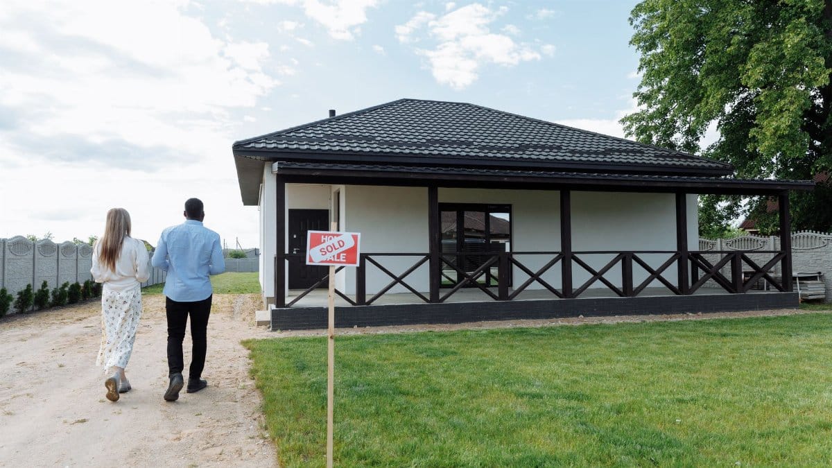 A couple walks towards their newly purchased home; a sign indicates the house is sold.