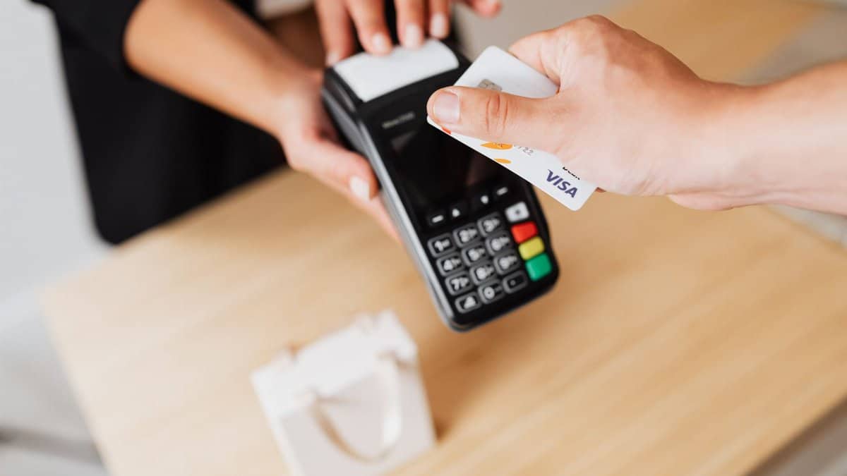 Close-up of hands using a contactless payment terminal with a credit card indoors.
