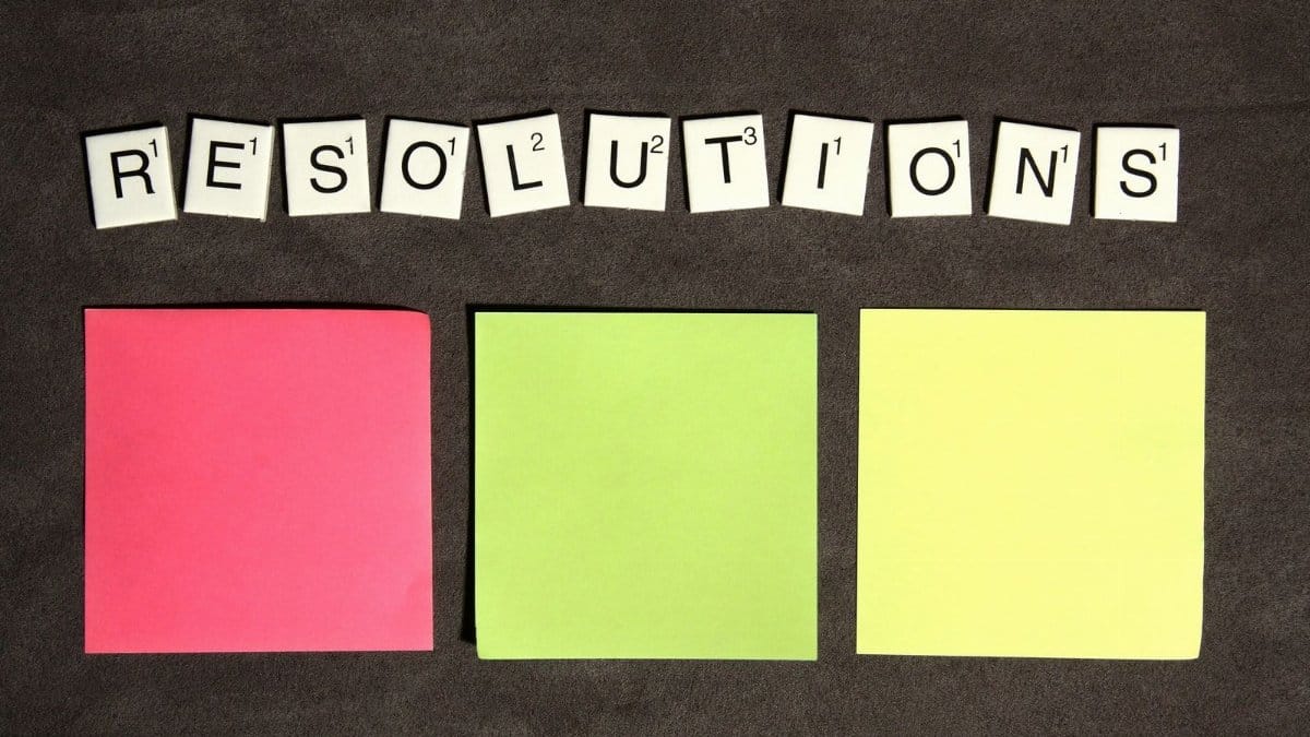 Scrabble tiles spelling 'Resolutions' above colorful sticky notes for goal setting.