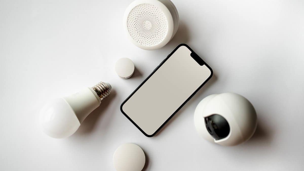 Flat lay of smartphone and smart home devices on a white backdrop, showcasing modern technology.