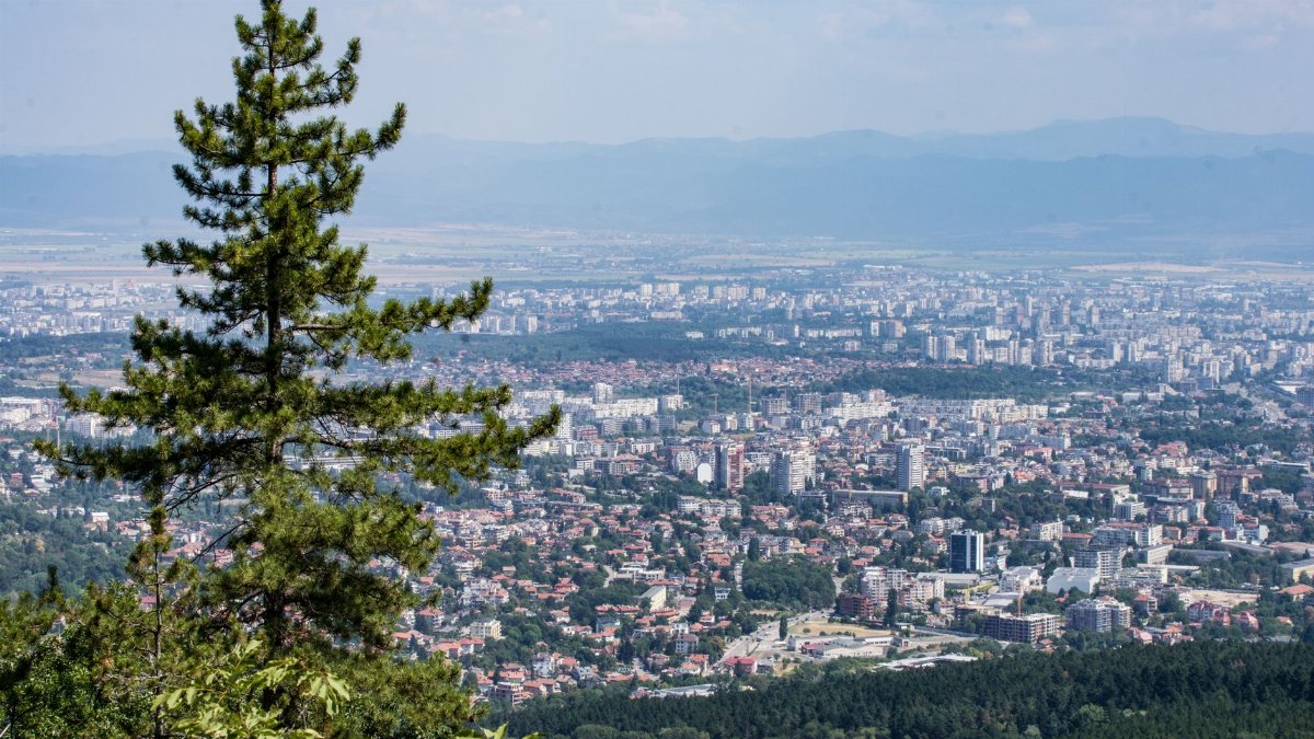Expansive aerial view over Sofia city from Vitosha Mountain with lush greenery and distant cityscape.