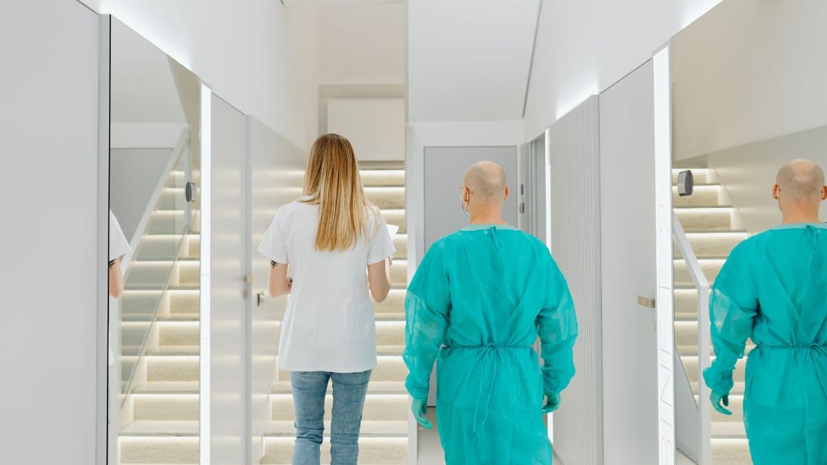 Two medical practitioners walking down a bright clinic hallway with reflections in mirrors.