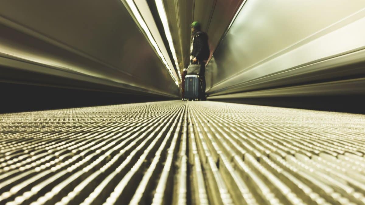 A traveler with luggage on a moving walkway in a modern airport corridor.
