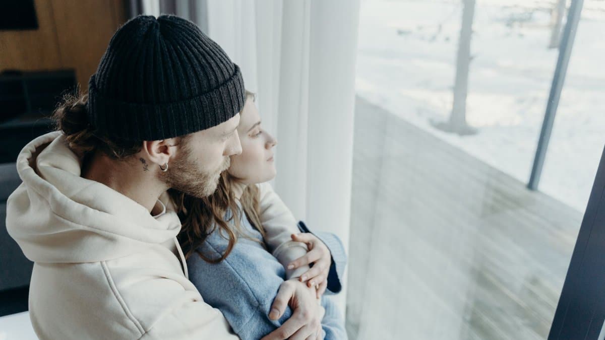 Warm embrace of a couple enjoying the tranquil snowy view through a large window.
