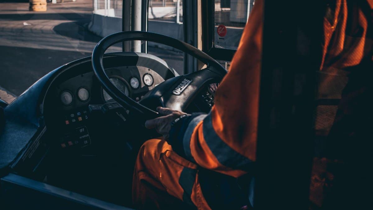 Bus driver operating vehicle from the cockpit in an industrial setting, showcasing control and focus.