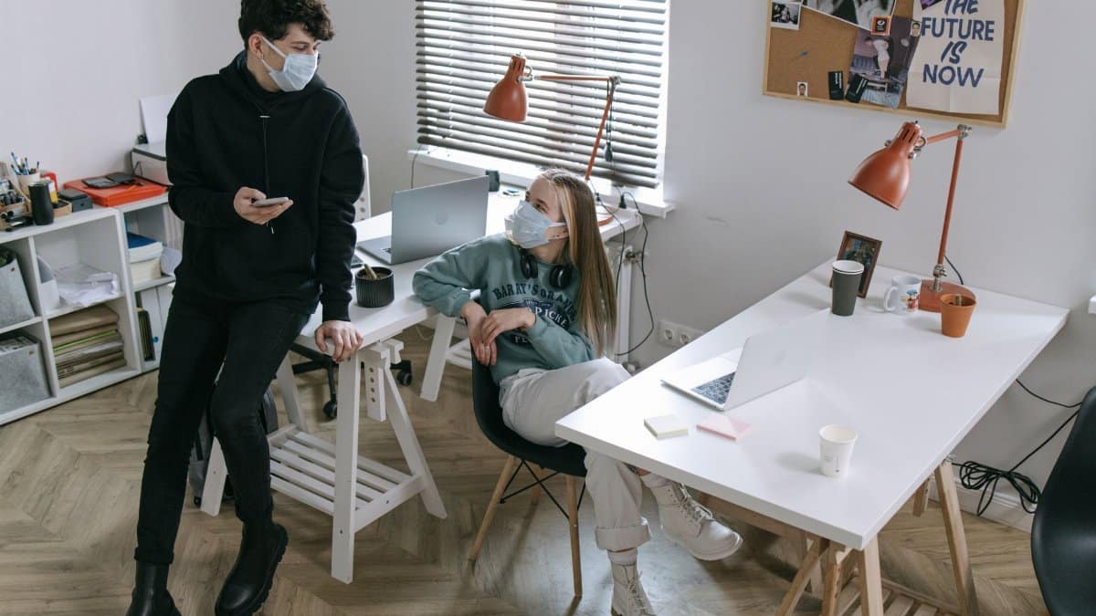 Young professionals wearing masks working at a modern office desk during COVID-19.