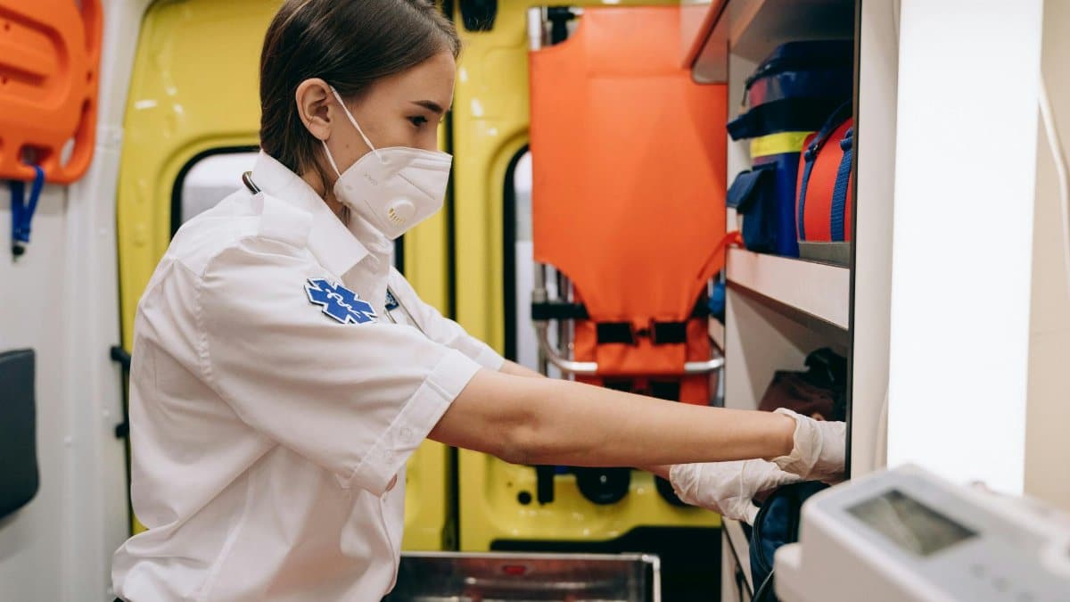 A female paramedic wearing a mask organizes supplies inside an ambulance, focusing on readiness.