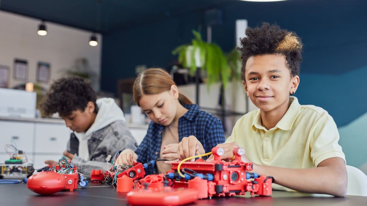 Three kids collaborating on a robotics project in a modern classroom setting.