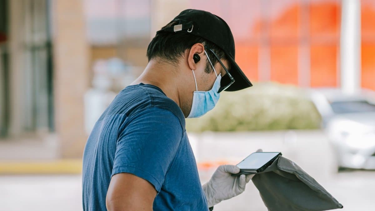 Man in mask and gloves using smartphone outdoors, focused and connected.