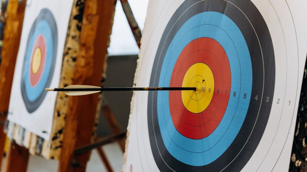 An arrow hits the bullseye on a colorful target in an indoor archery range.