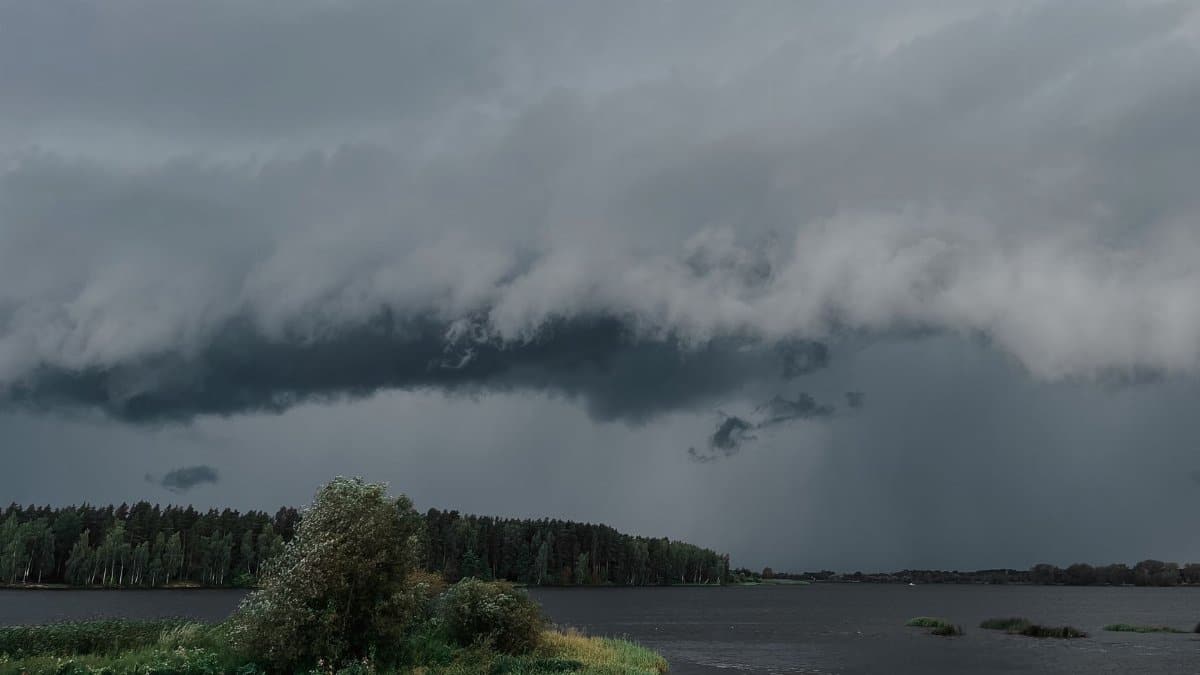 A powerful storm cloud formation looms over a tranquil lake and forest, capturing nature's dynamic beauty.