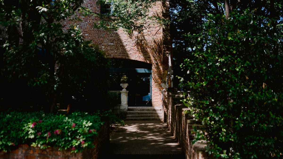 A picturesque brick house entrance surrounded by lush greenery and stone steps, evoking a serene atmosphere.