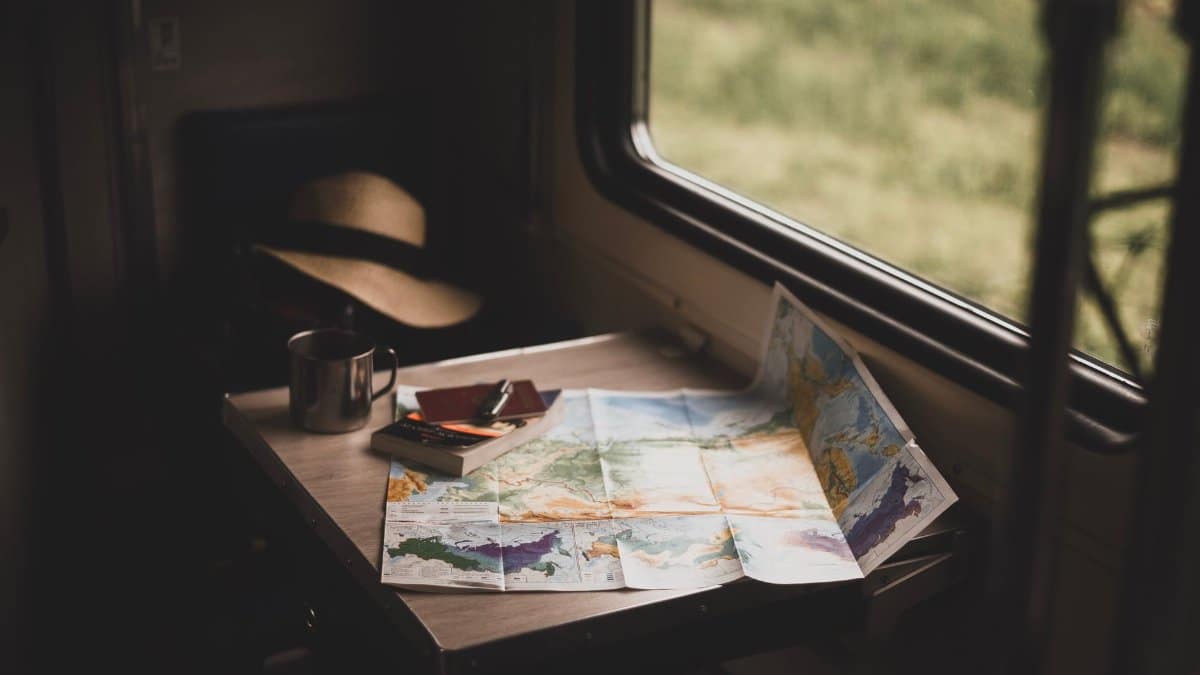 A serene train ride setup with a world map, mug, and hat on a table, suggesting travel plans.