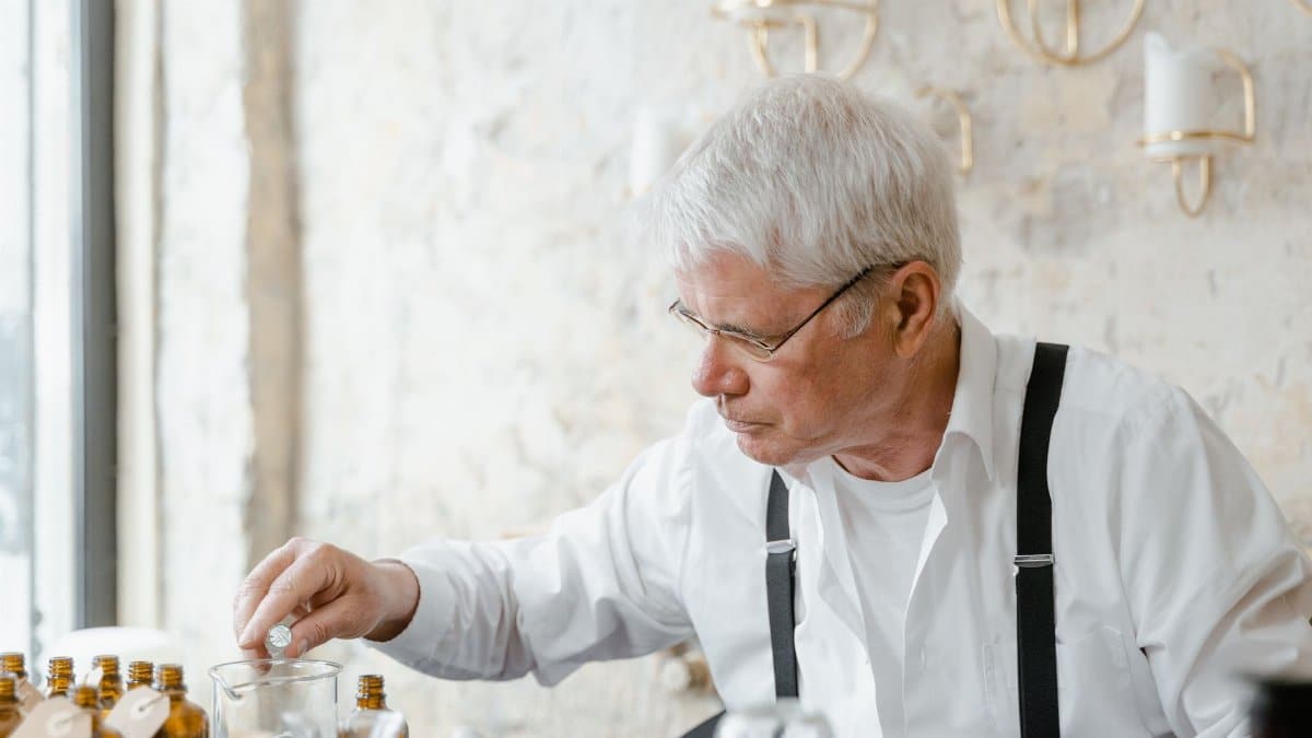 Senior man with white hair and eyeglasses working with perfume bottles in an indoor setting.