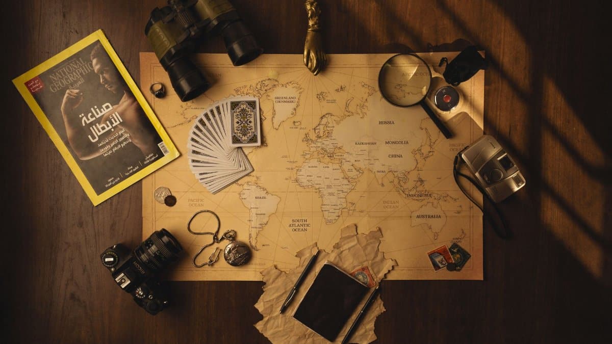 A styled flat lay of travel essentials including a map, camera, and binoculars.