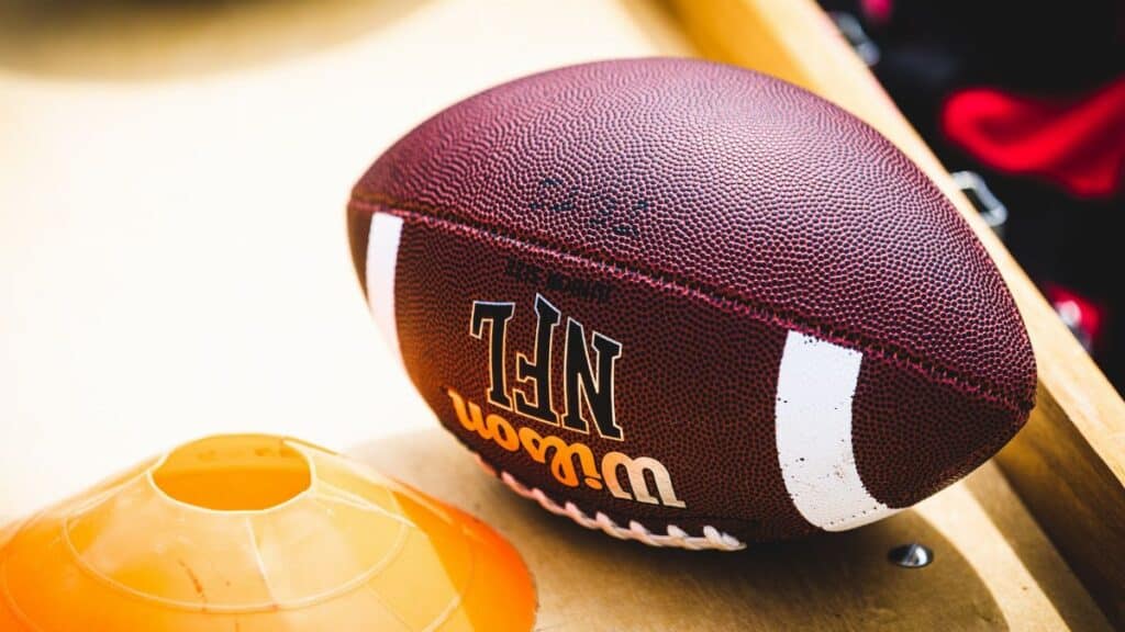 An American football placed on a training bench next to an orange training cone, ideal for sports concept.