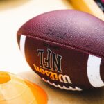 An American football placed on a training bench next to an orange training cone, ideal for sports concept.