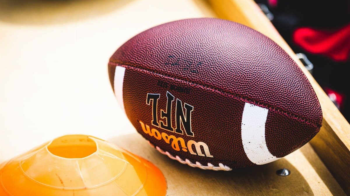 An American football placed on a training bench next to an orange training cone, ideal for sports concept.