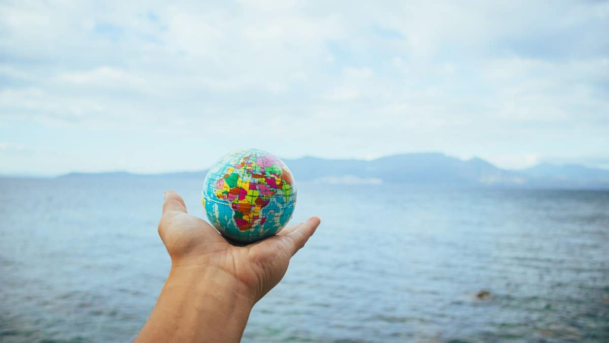 A hand holds a small globe with a scenic ocean backdrop, symbolizing global exploration.