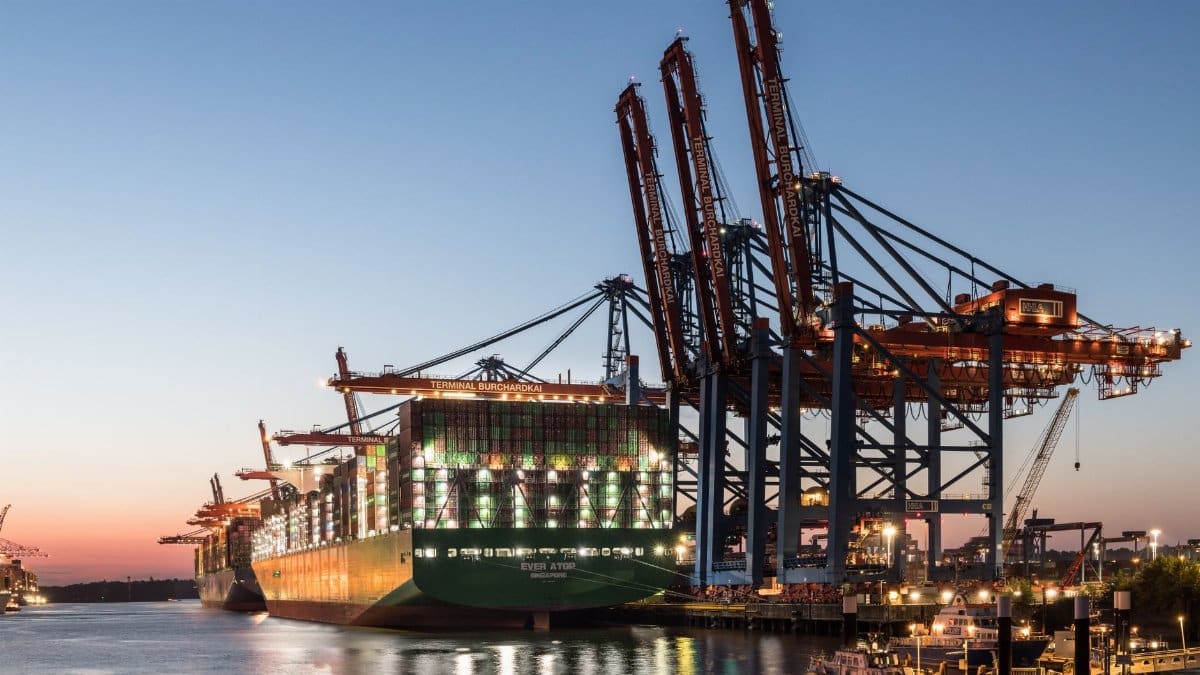 A large container ship at the Hamburg port with cranes during twilight, showcasing global trade.